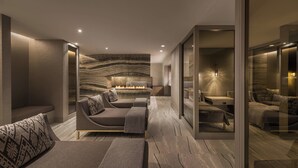 A modern living room with a sofa, a coffee table, and a fireplace. There is a glass partition and a view of another room.