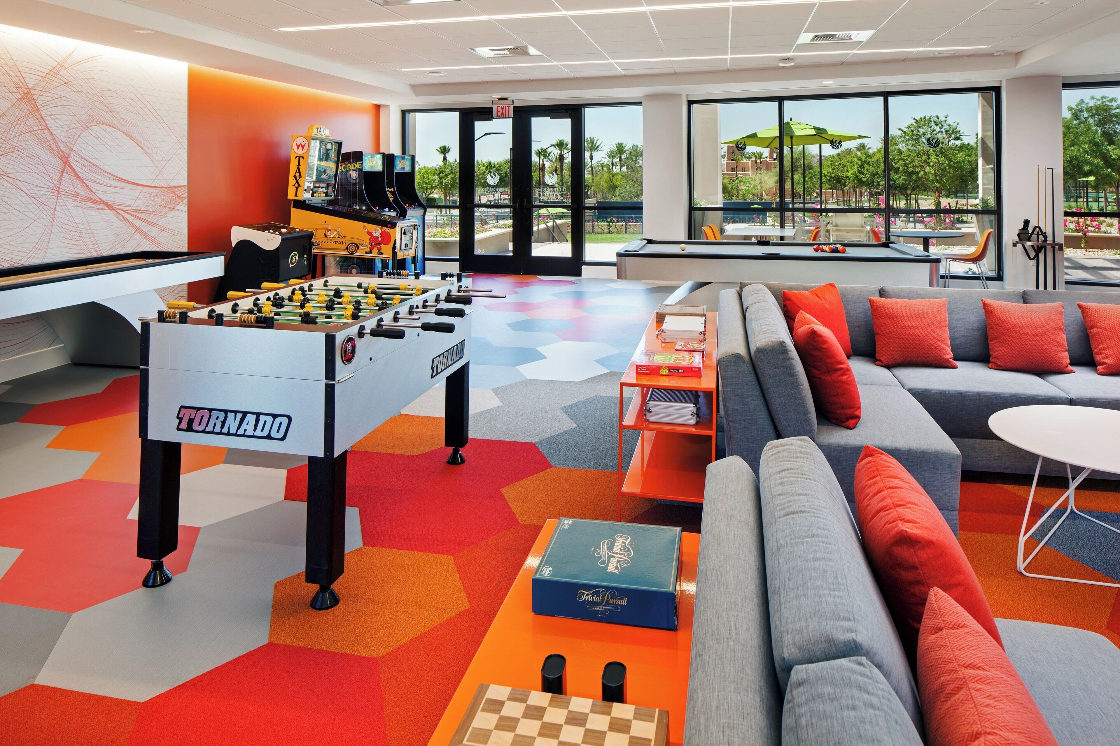A modern indoor space with a foosball table labeled "TORNADO," a pool table, and a sofa with orange cushions.