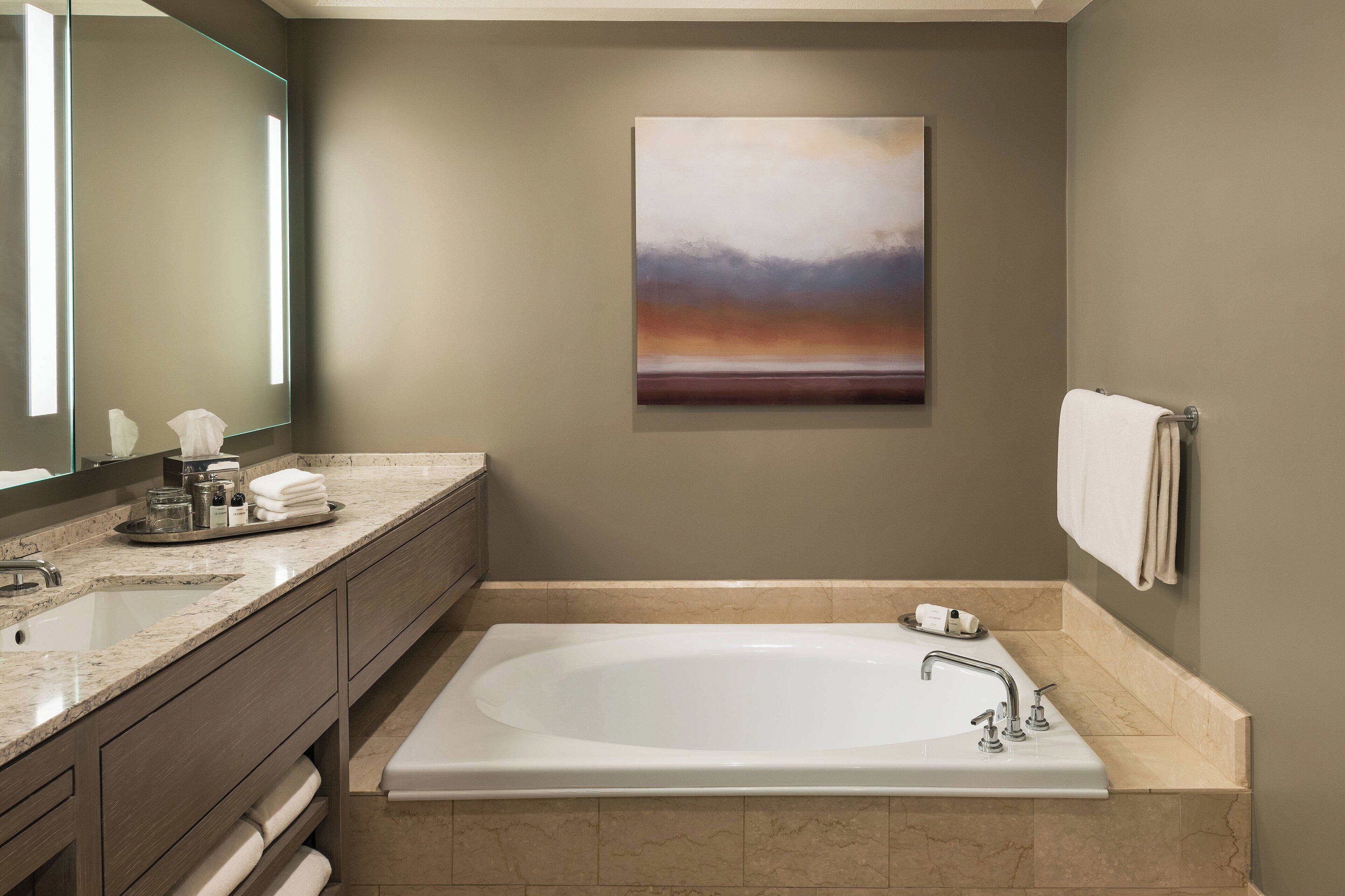 A modern bathroom with a large bathtub, a vanity with a mirror, and a towel rack.