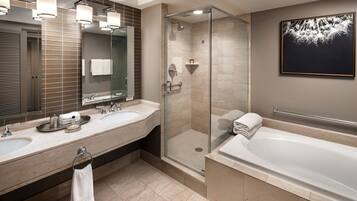 A modern bathroom with two sinks, a glass-enclosed shower, a large bathtub, and a framed artwork on the wall.
