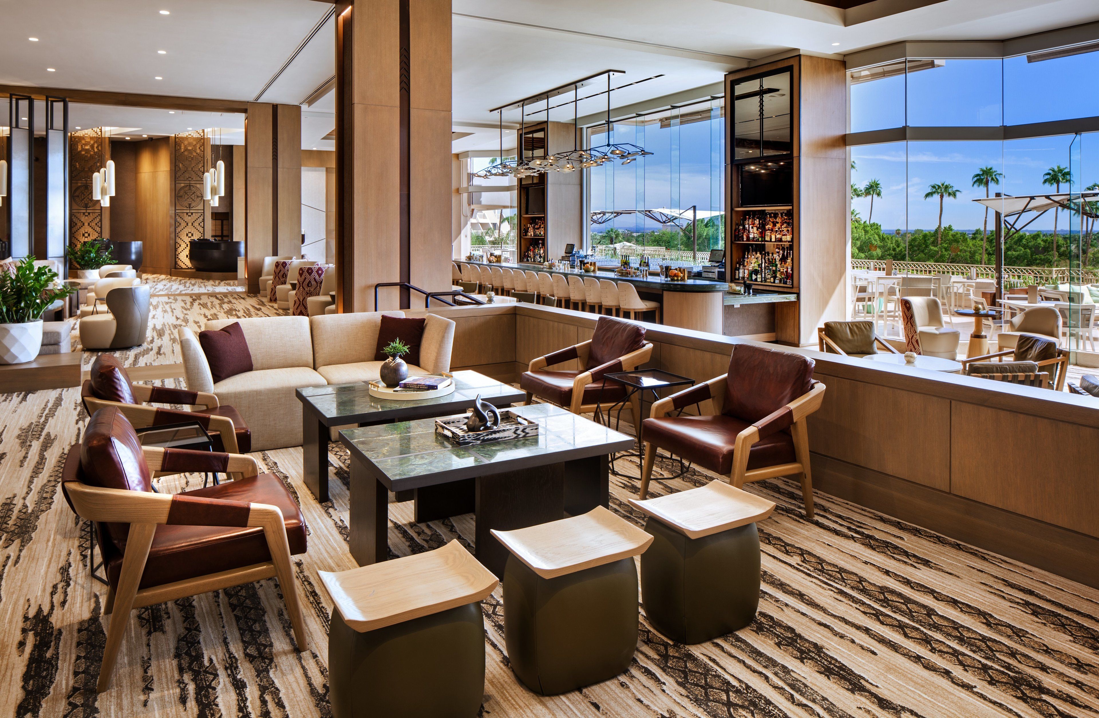 A modern hotel lobby with a bar, seating area, and large windows offering a view of palm trees.