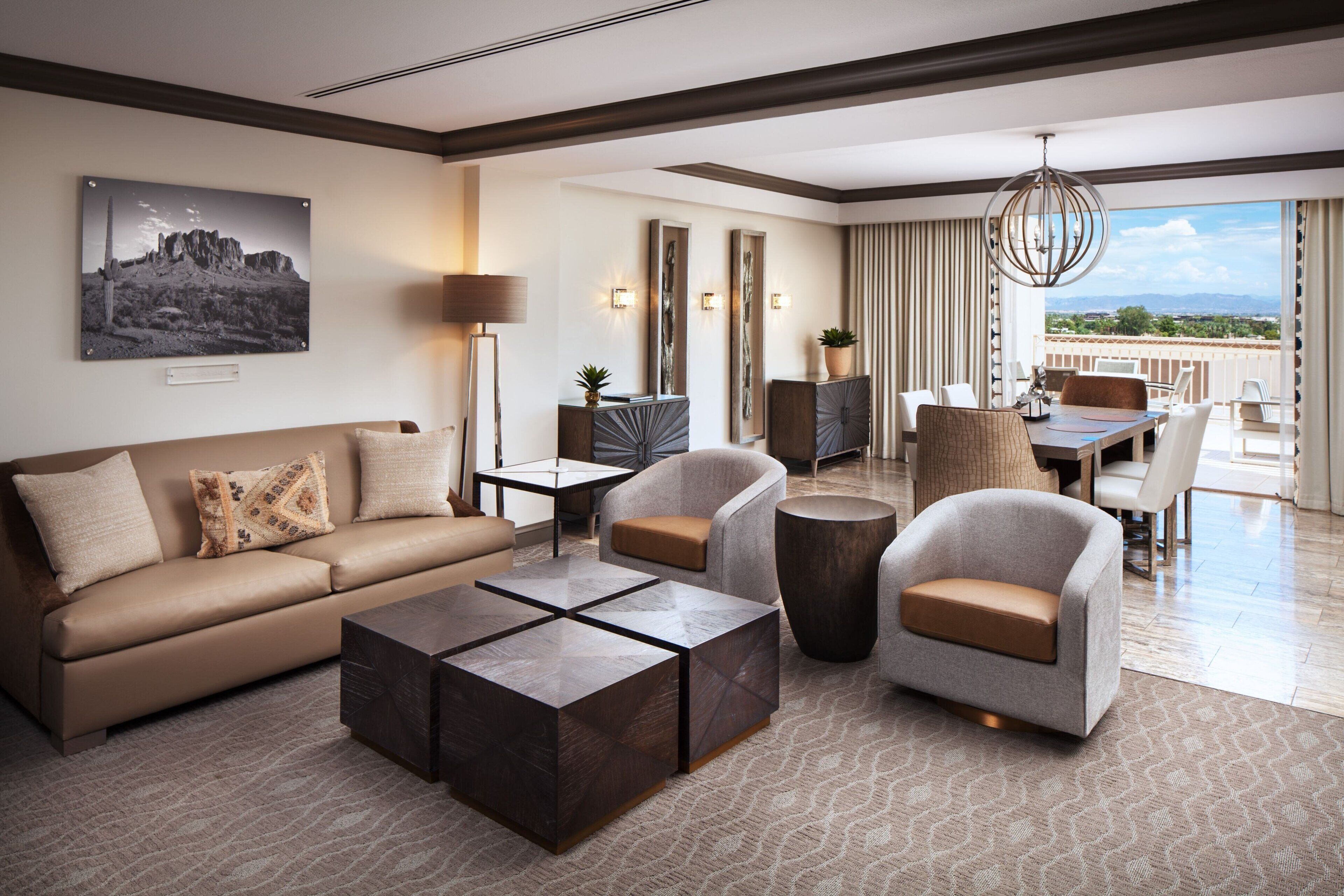 Een moderne hotelkamer met een bank, fauteuils, een salontafel, een eethoek en een balkon met uitzicht.