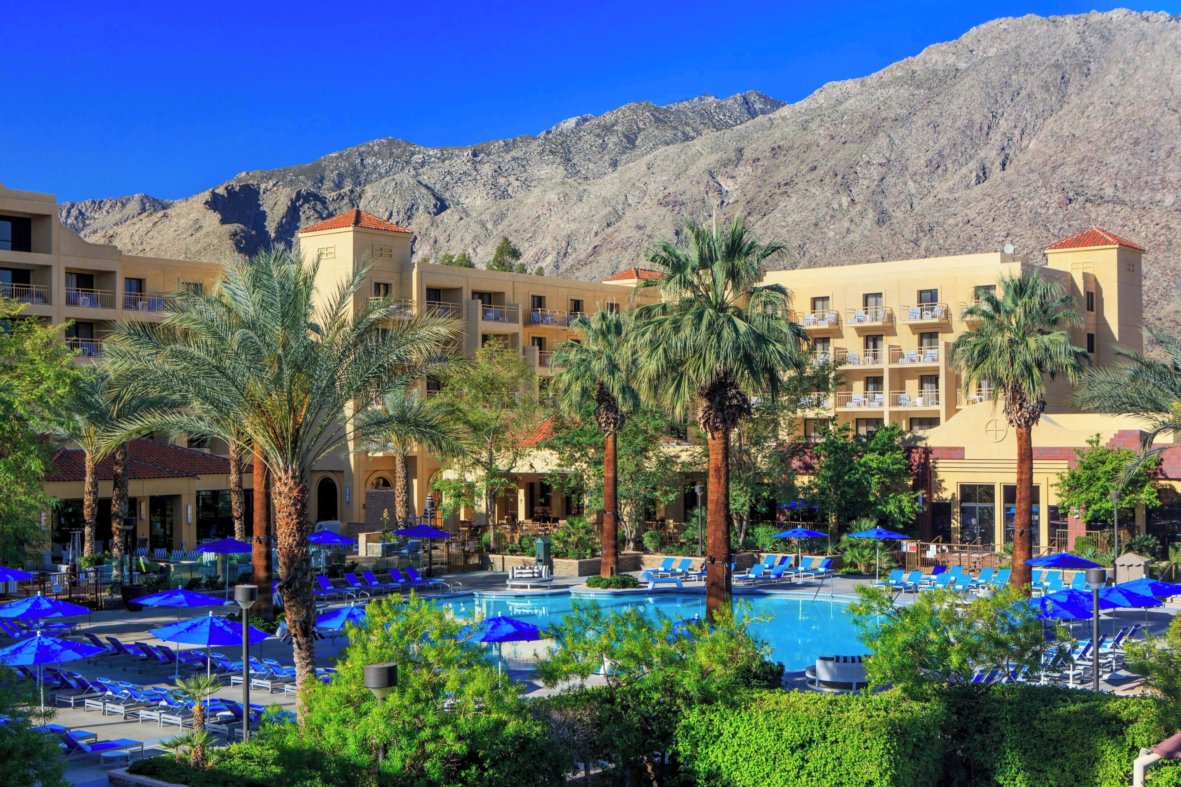 Un hotel con piscina, palmeras y montañas al fondo.