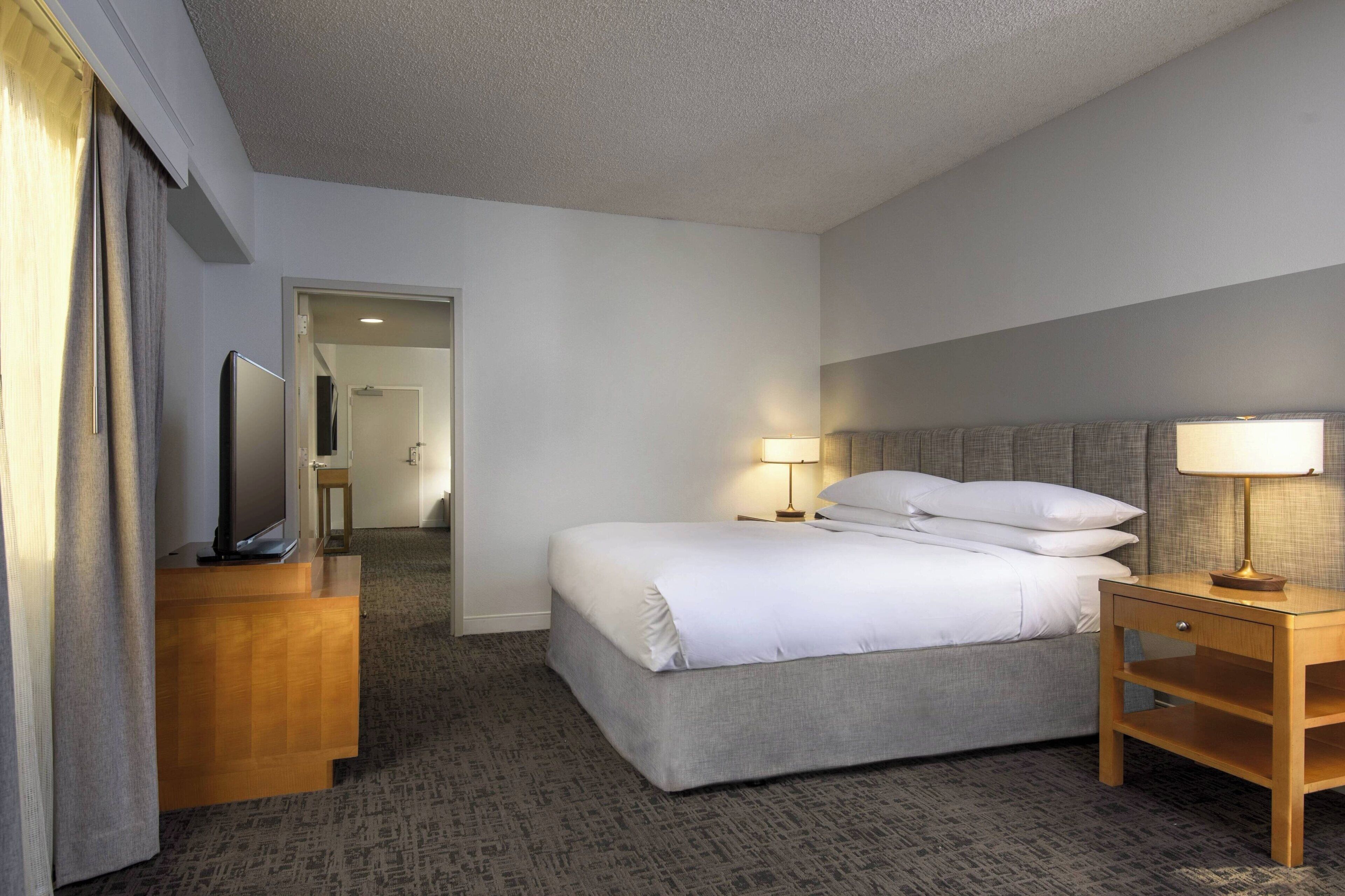 A hotel room with a bed, bedside tables, a TV, and a lamp.