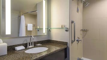 Ein modernes Badezimmer mit einer Granit-Arbeitsplatte, einem weißen Waschbecken, einer Duschkabine aus Glas und einem großen Spiegel.