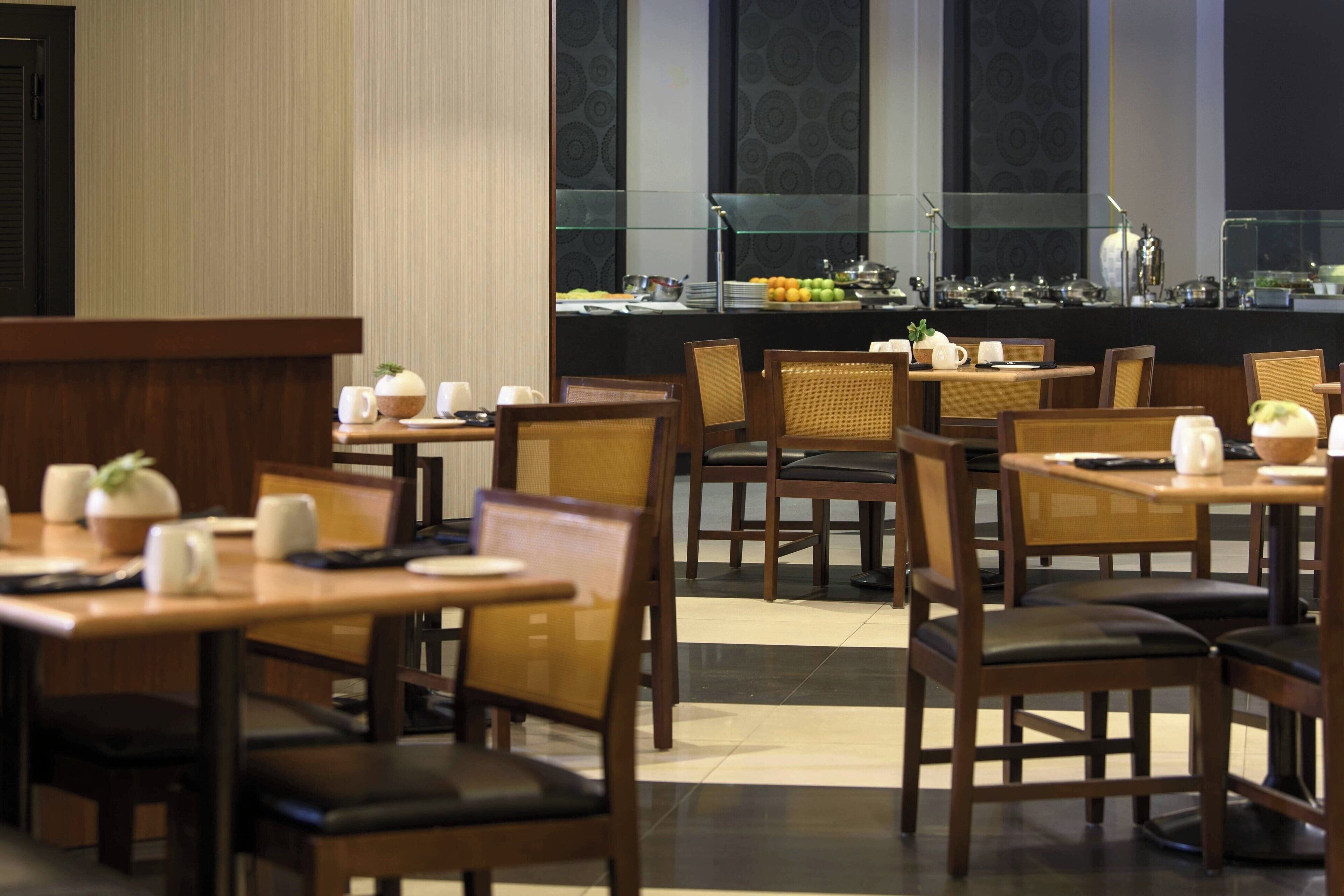 A restaurant with wooden tables and chairs, a buffet area with fruits and dishes, and a modern interior design.