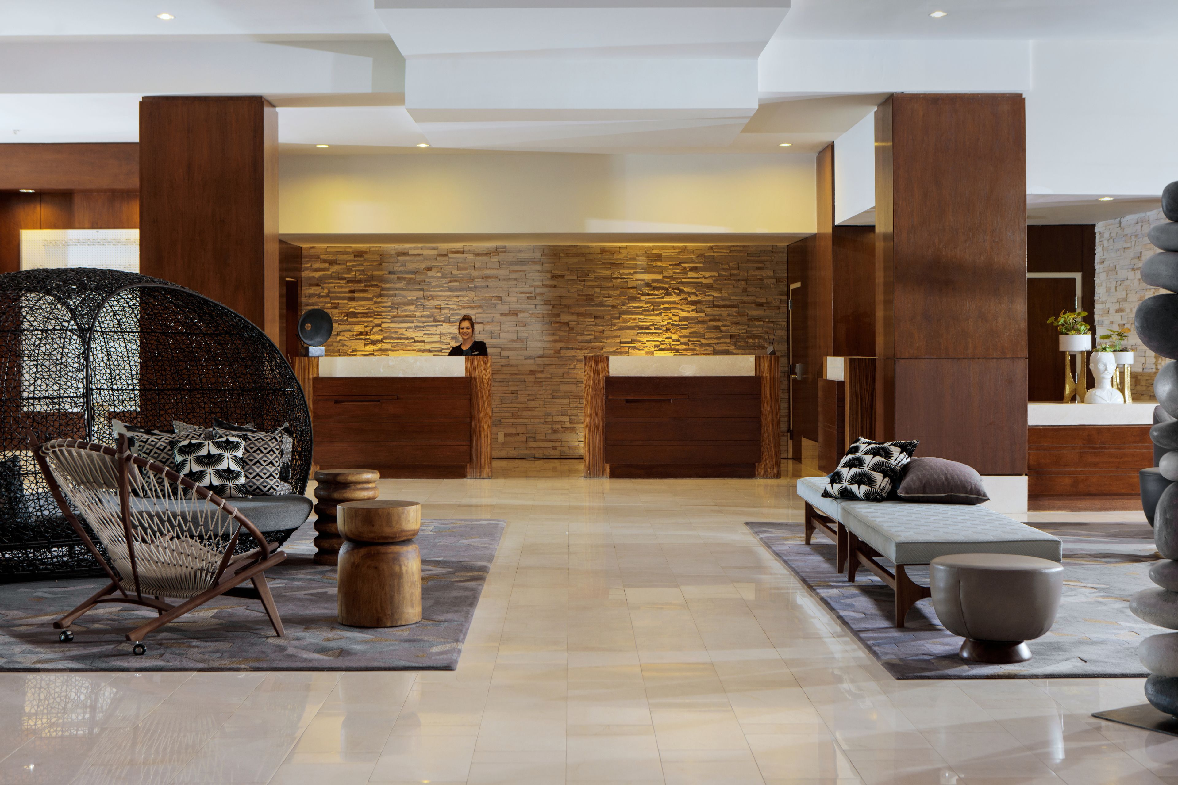 A modern lobby with a stone wall, wooden reception desk, seating area, and a decorative stone sculpture.
