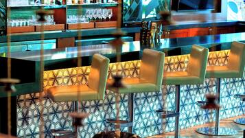 A bar area with a patterned wall, bar stools, and a variety of bottles and glasses on shelves.