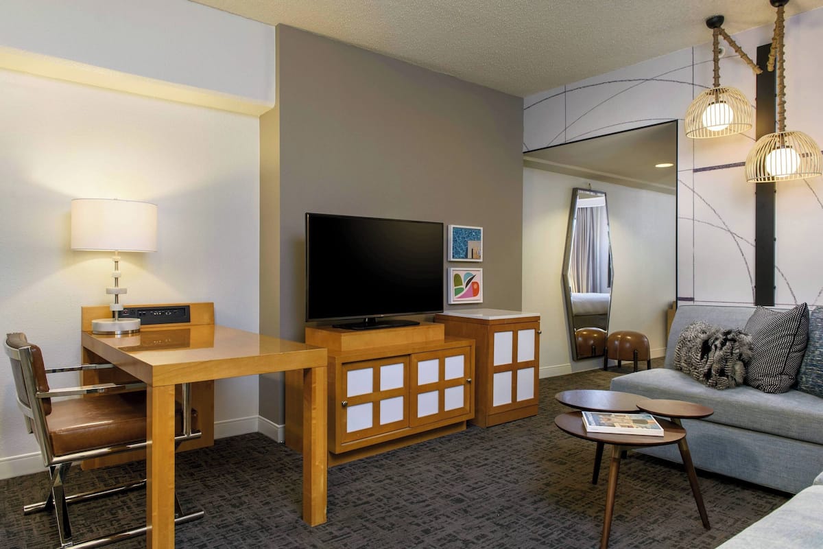 A hotel room with a wooden desk, a television, a sofa, and a small table.