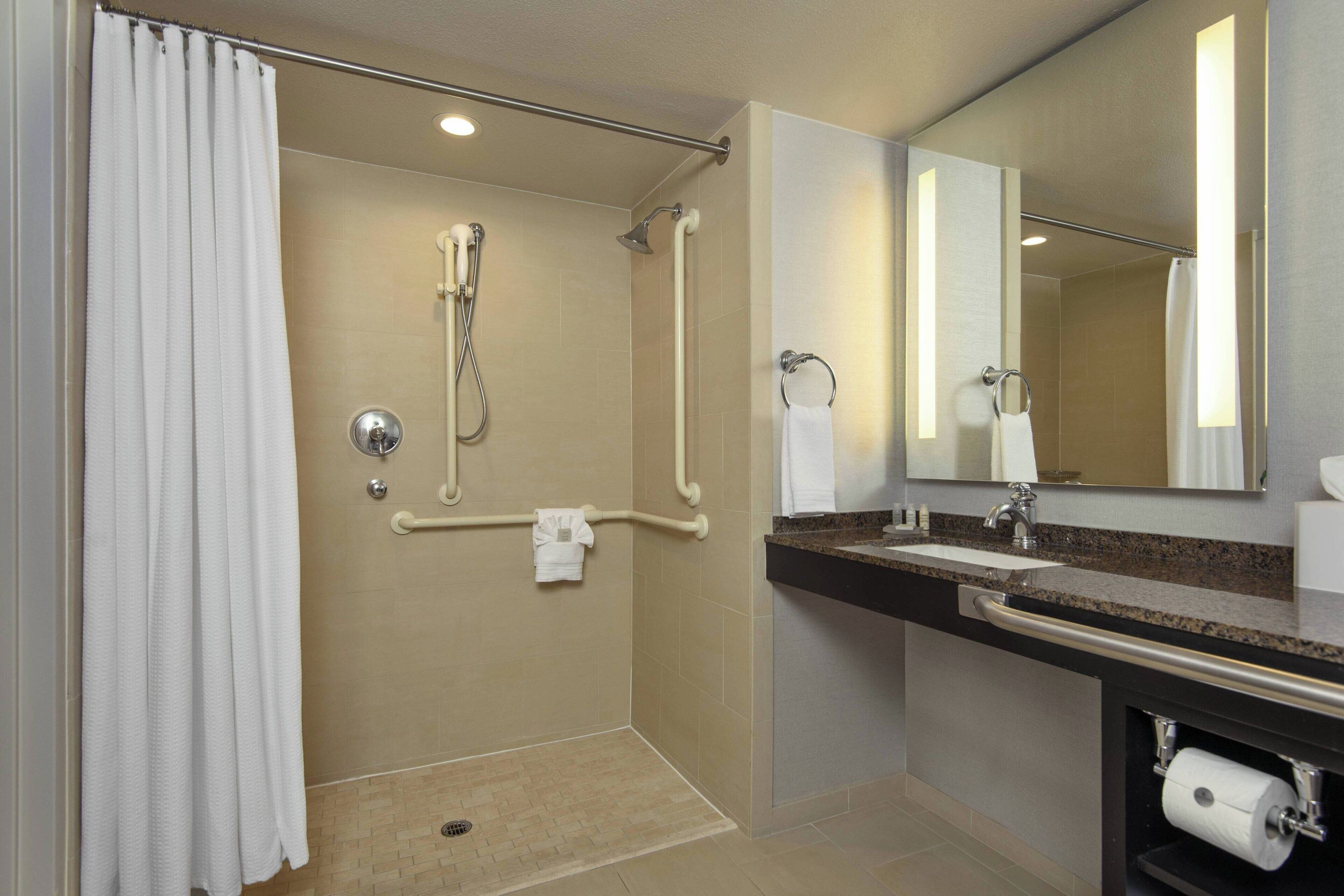 A modern bathroom with a walk-in shower, grab bars, a sink with a towel rack, and a toilet paper holder.