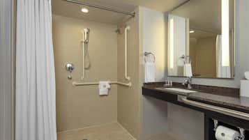 Une salle de bain moderne dotée d’une douche à l’italienne, de barres d’appui, d’un lavabo avec un porte-serviettes et d’un support à papier toilette.