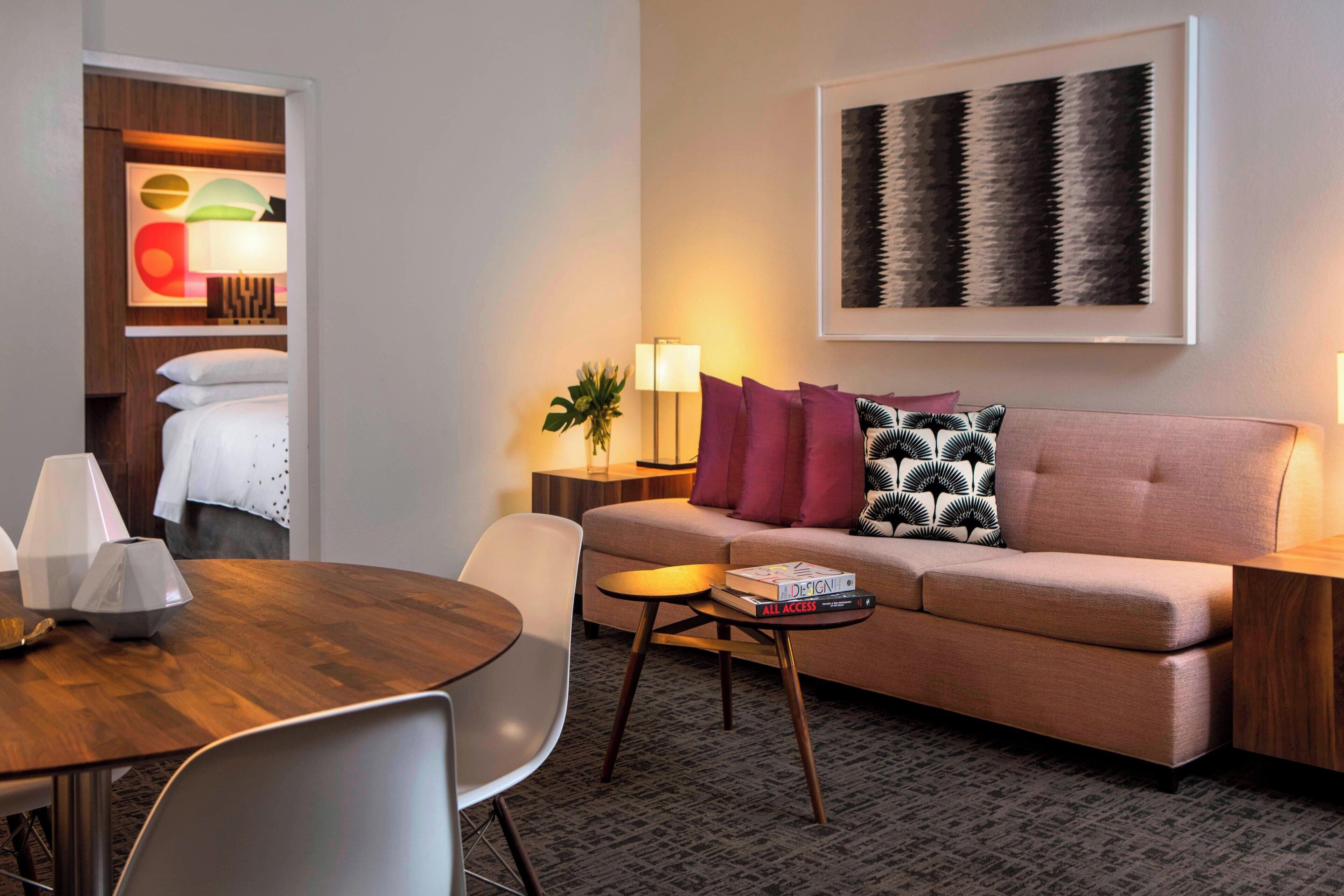 Ett modernt hotellrum med en soffa, ett matbord och en lampa.