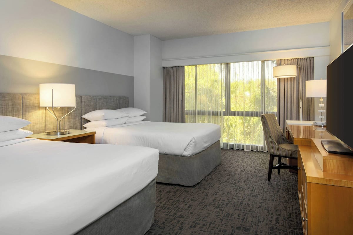 A hotel room with two beds, a desk, a chair, and a TV.
