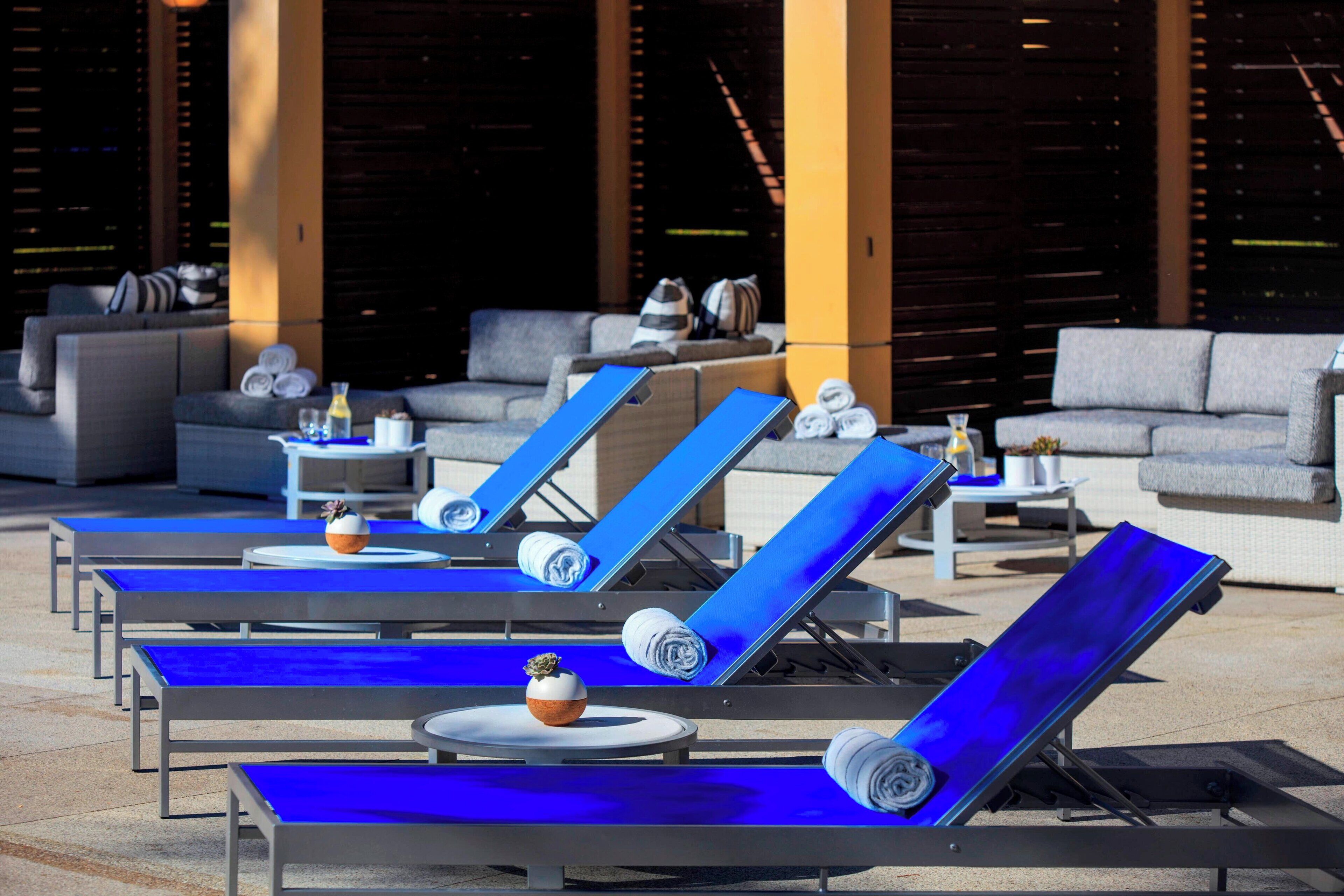 A poolside area with sun loungers, a sofa, and a small table with a vase and bottle.