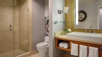 A modern bathroom with a glass-enclosed shower, a white toilet, a large sink with a mirror, and neatly rolled towels on a shelf.