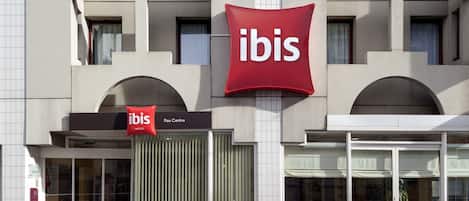 A hotel with a prominent red 'ibis' sign, a glass entrance, and a 'Pau Centre' sign.