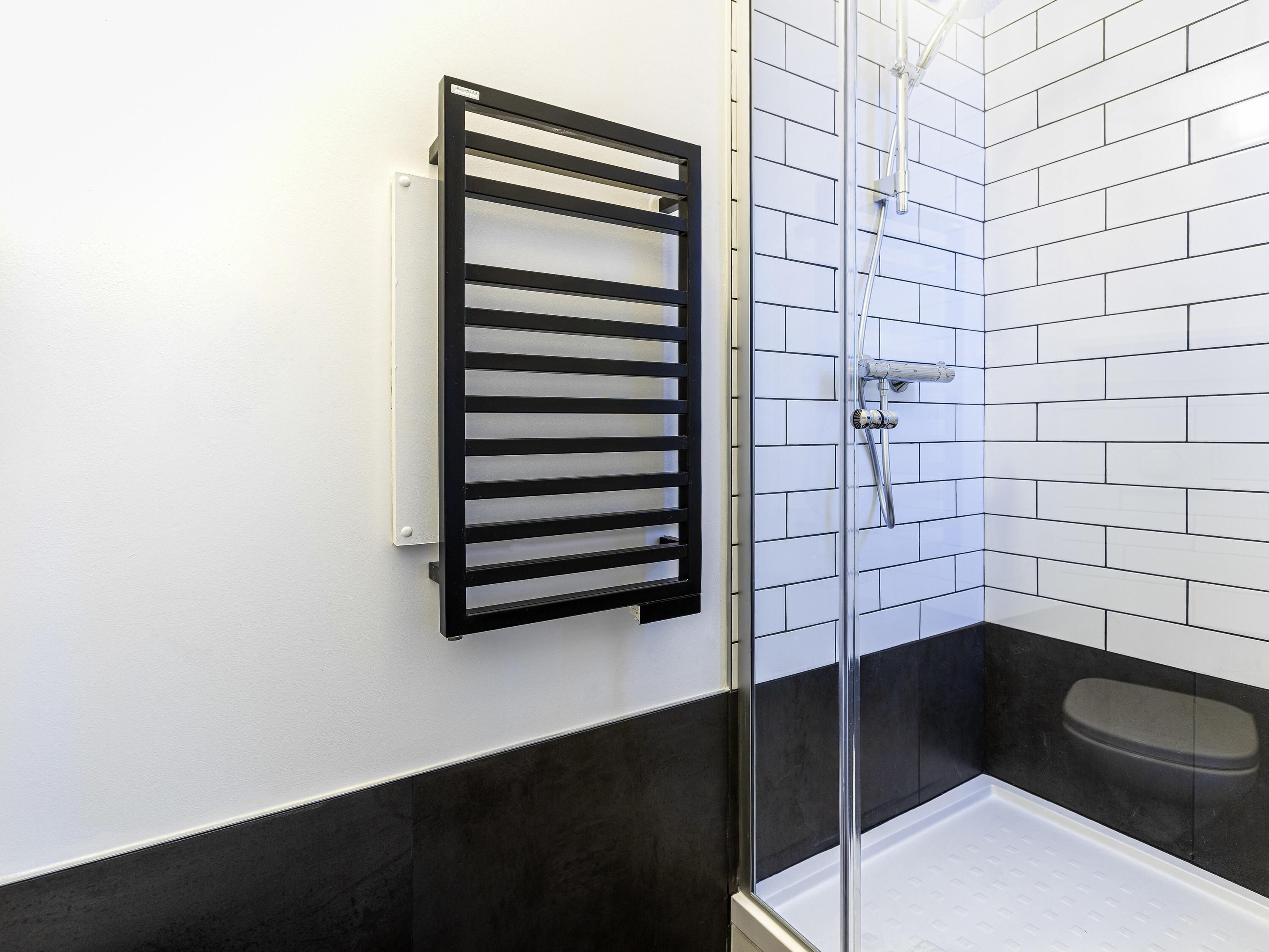 A bathroom with a glass shower enclosure, a black towel rack, and a white tiled wall.