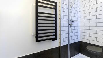 A bathroom with a glass shower enclosure, a black towel rack, and a white tiled wall.
