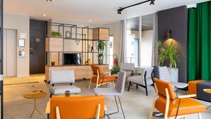 Un salon moderne avec des fauteuils orange et gris, un téléviseur et une bibliothèque.