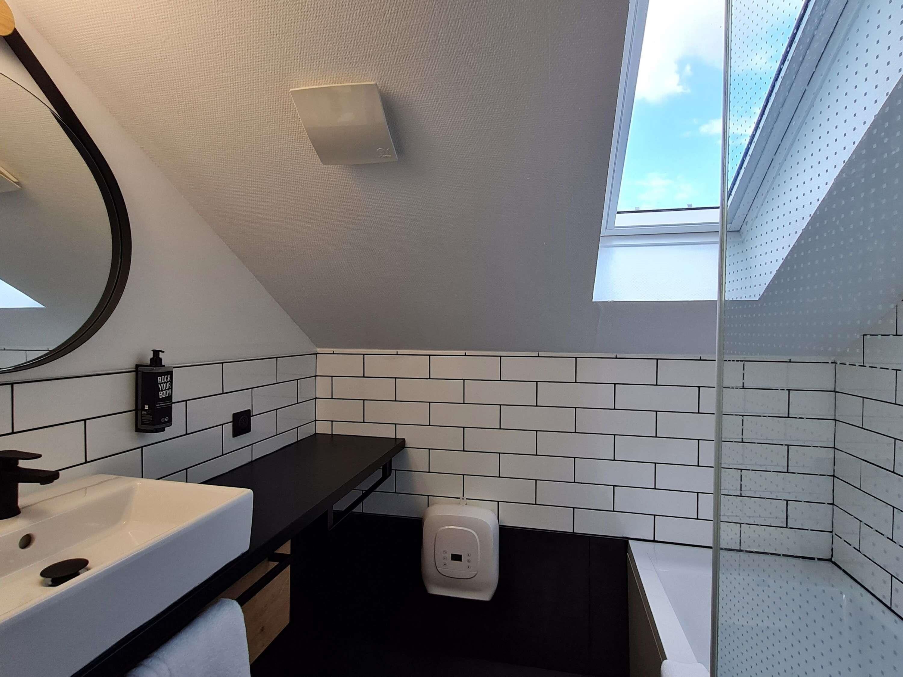A modern bathroom with a skylight, white tiled walls, a black countertop, and a white sink.