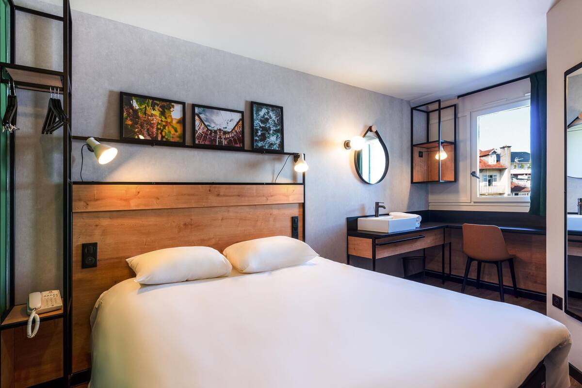 Una habitación de hotel con una cama grande, un escritorio con lavabo, un espejo y obras de arte en la pared.