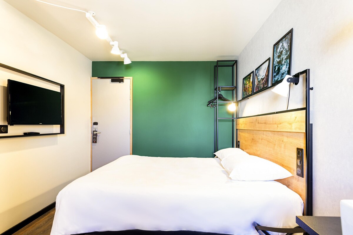 Une chambre d’hôtel avec un lit, une télévision, un bureau et un mur vert.