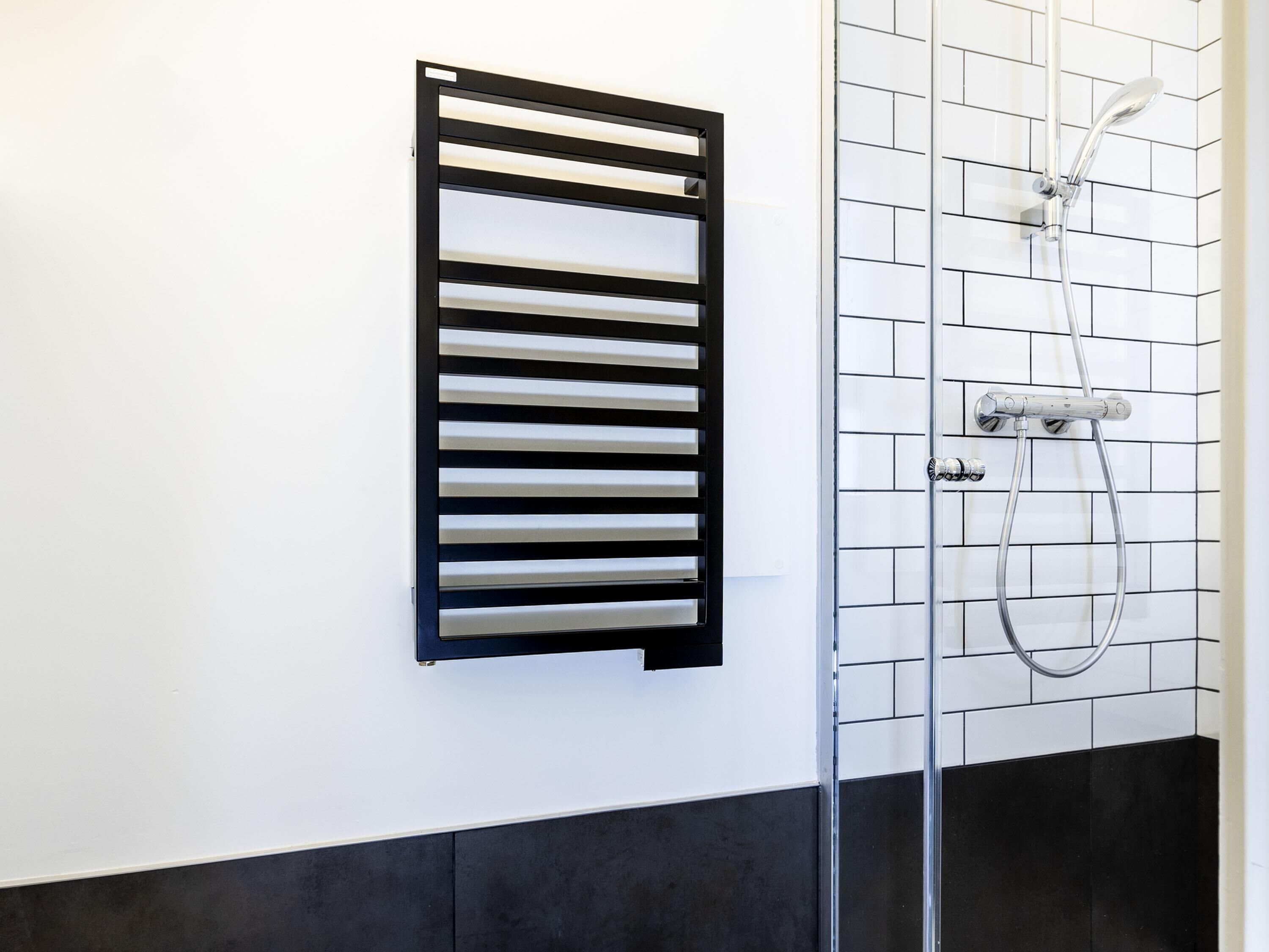 Ein Badezimmer mit schwarzem Handtuchhalter, einer Dusche mit Duschbrause und einer gefliesten Wand.