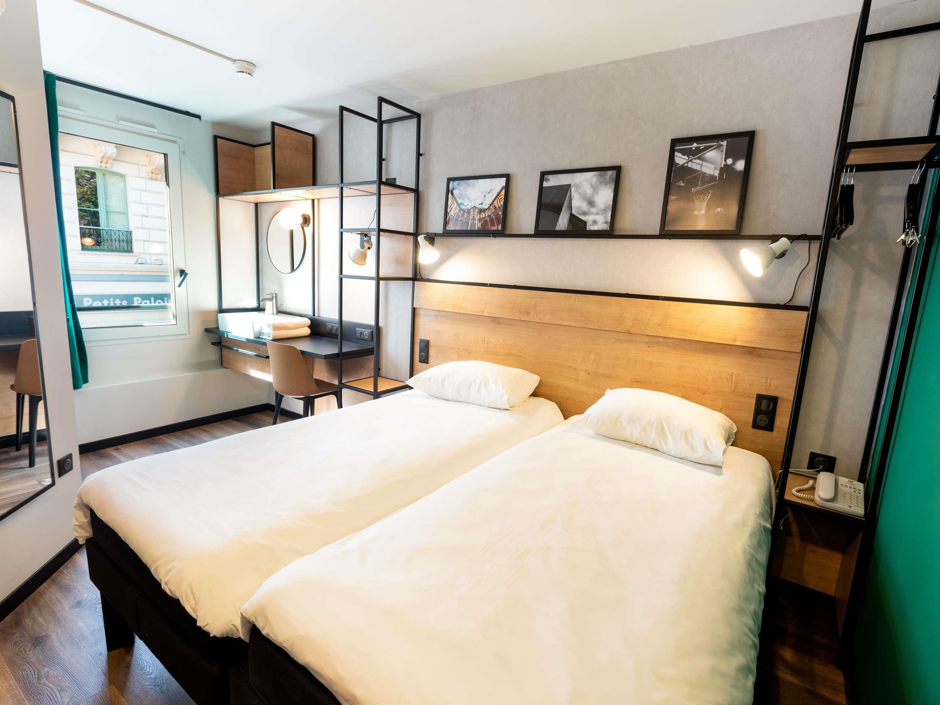 Una habitación de hotel con dos camas, un escritorio, una silla, un espejo y obras de arte en la pared.