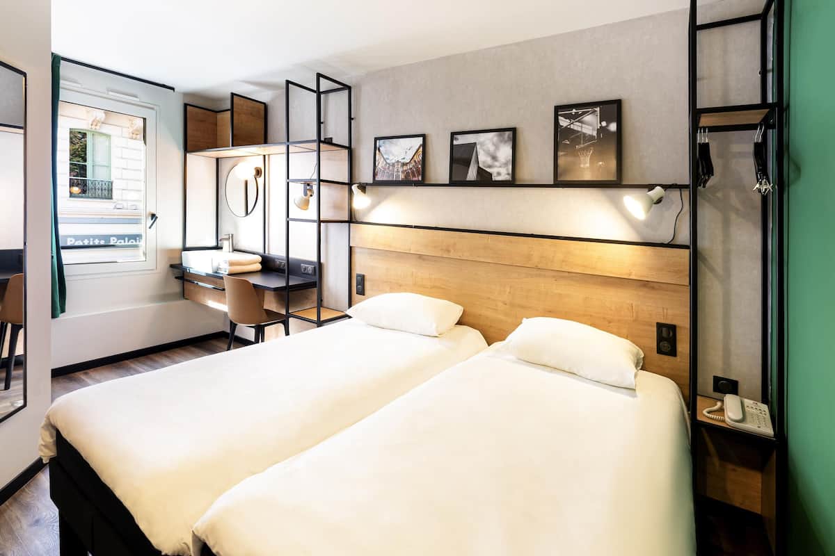 Habitación de hotel con dos camas, un escritorio, una silla, un teléfono y cuadros en la pared.