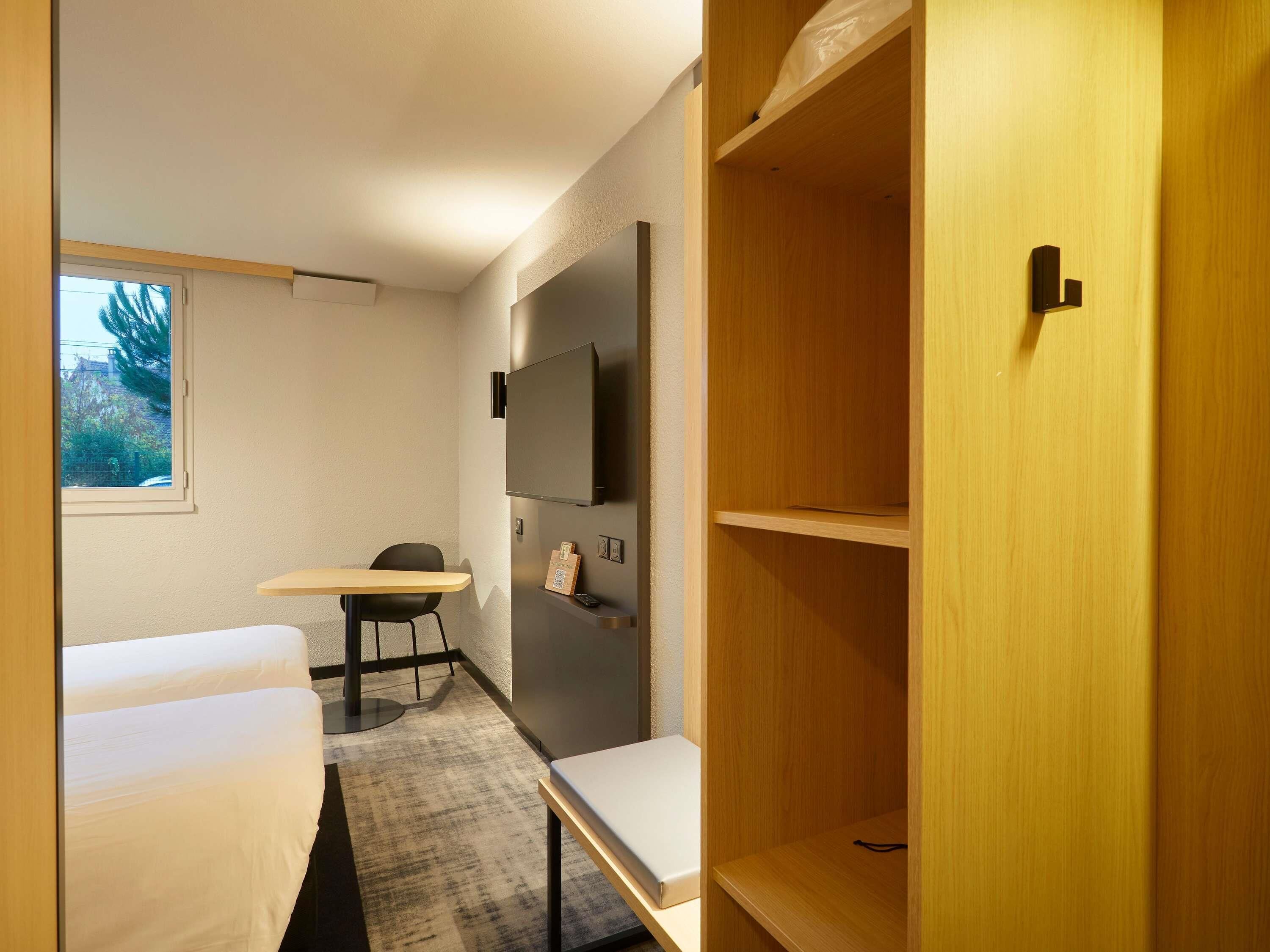 A small, modern room with a bed, a desk, a chair, a TV, and a wardrobe.