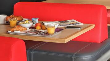 Un plateau de petit-déjeuner comprenant des croissants, des fruits, du jus de fruits et un journal.