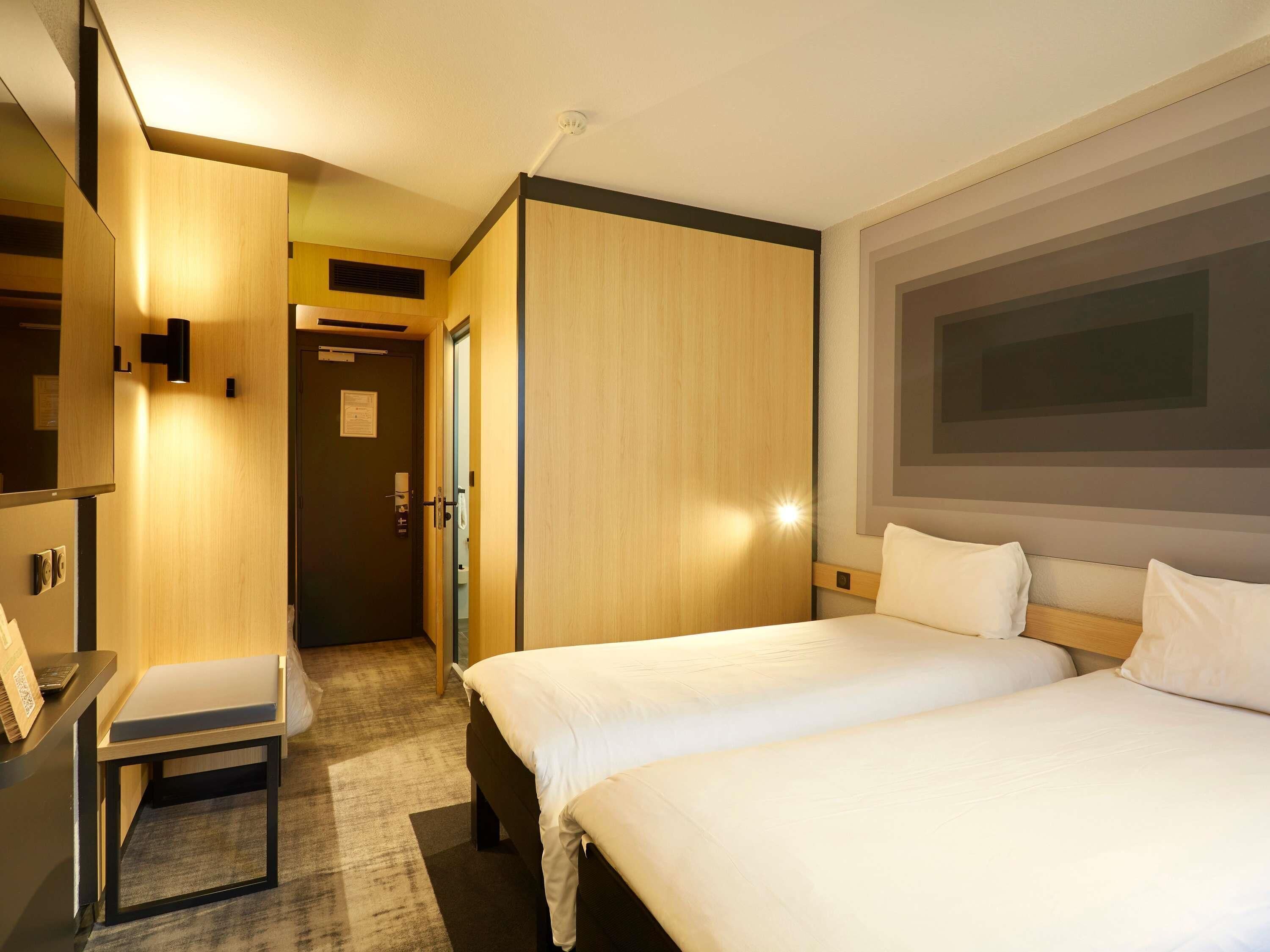 A hotel room with two beds, a desk, a chair, and a large window.