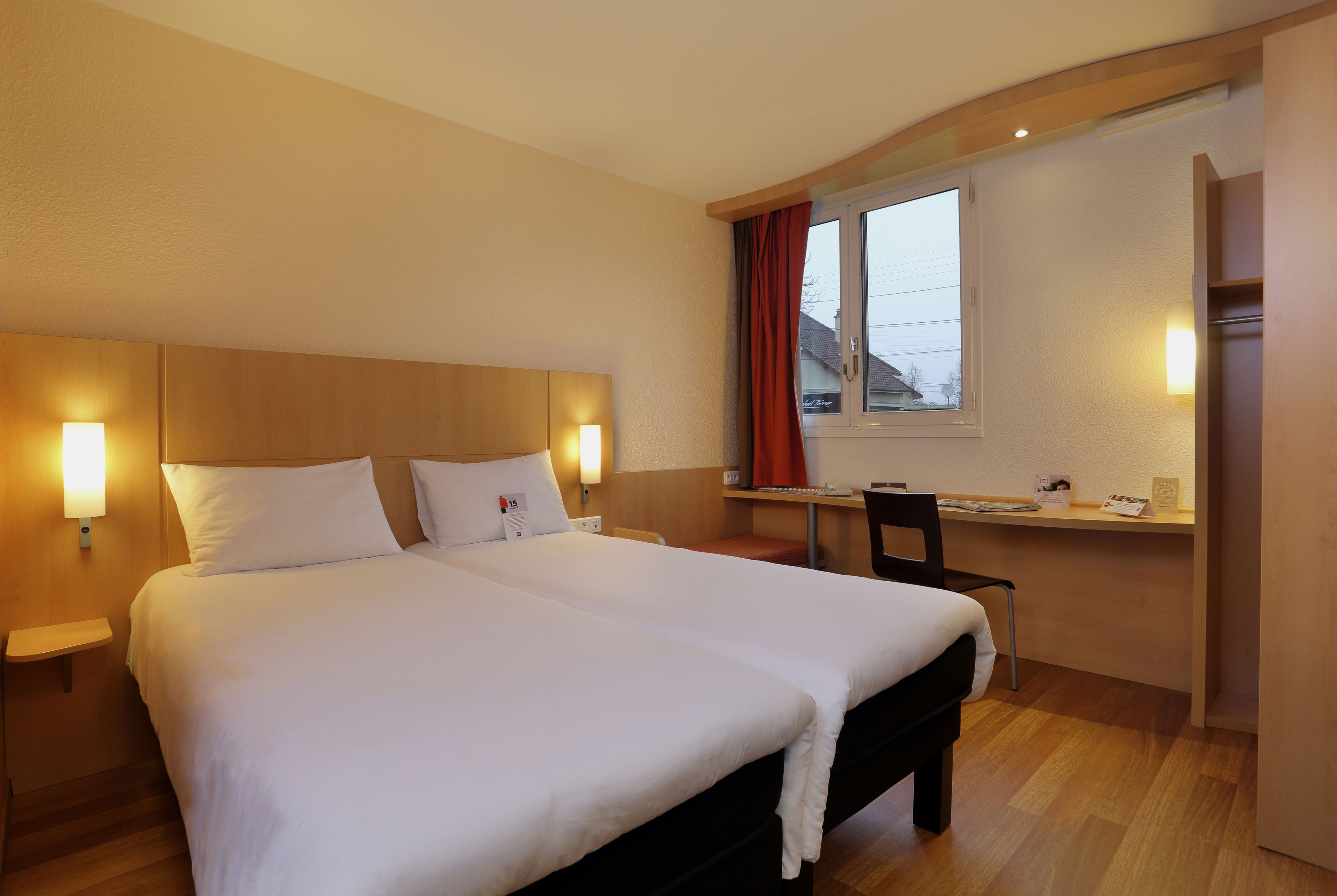 A hotel room with a large bed, bedside tables with lamps, a desk with a chair, and a window with curtains.
