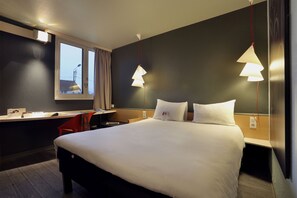 Habitación de hotel con una cama grande, un escritorio y una silla. Cuenta con una ventana con cortinas, una lámpara de pared y una lámpara colgante.