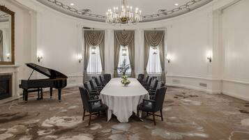 A formal dining room with a round table, black chairs, a grand piano, and a chandelier.