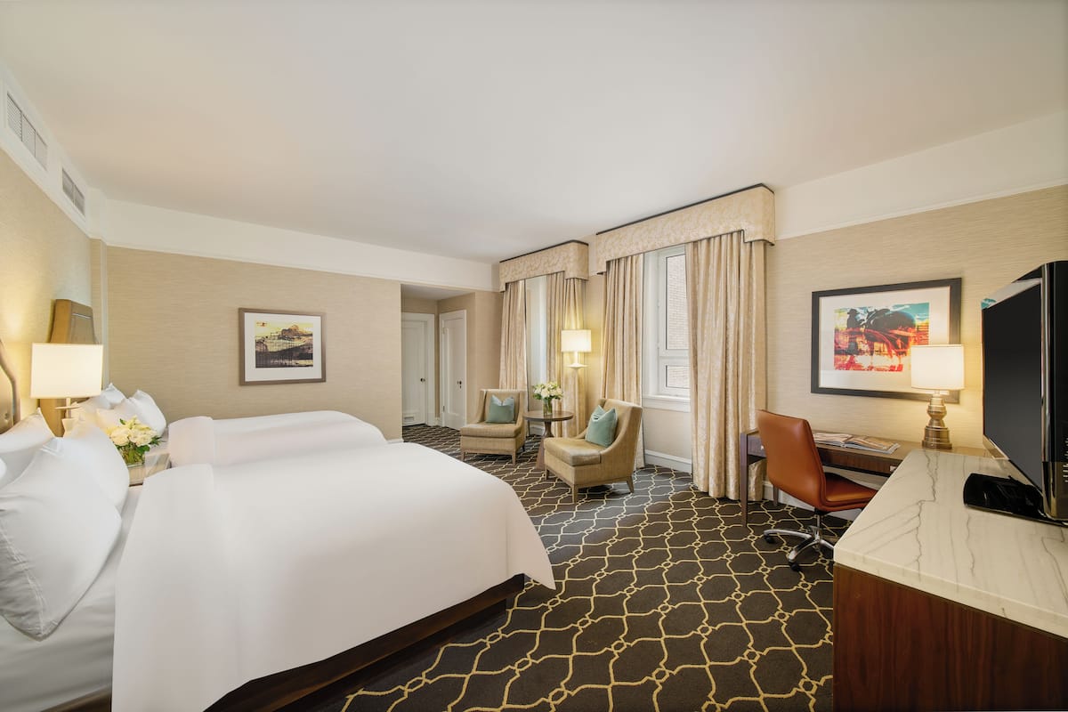 A hotel room with a large bed, two armchairs, a desk with a computer, and a television.