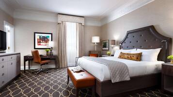 Una habitación de hotel con una cama grande, un escritorio con silla, un televisor y una alfombra estampada.