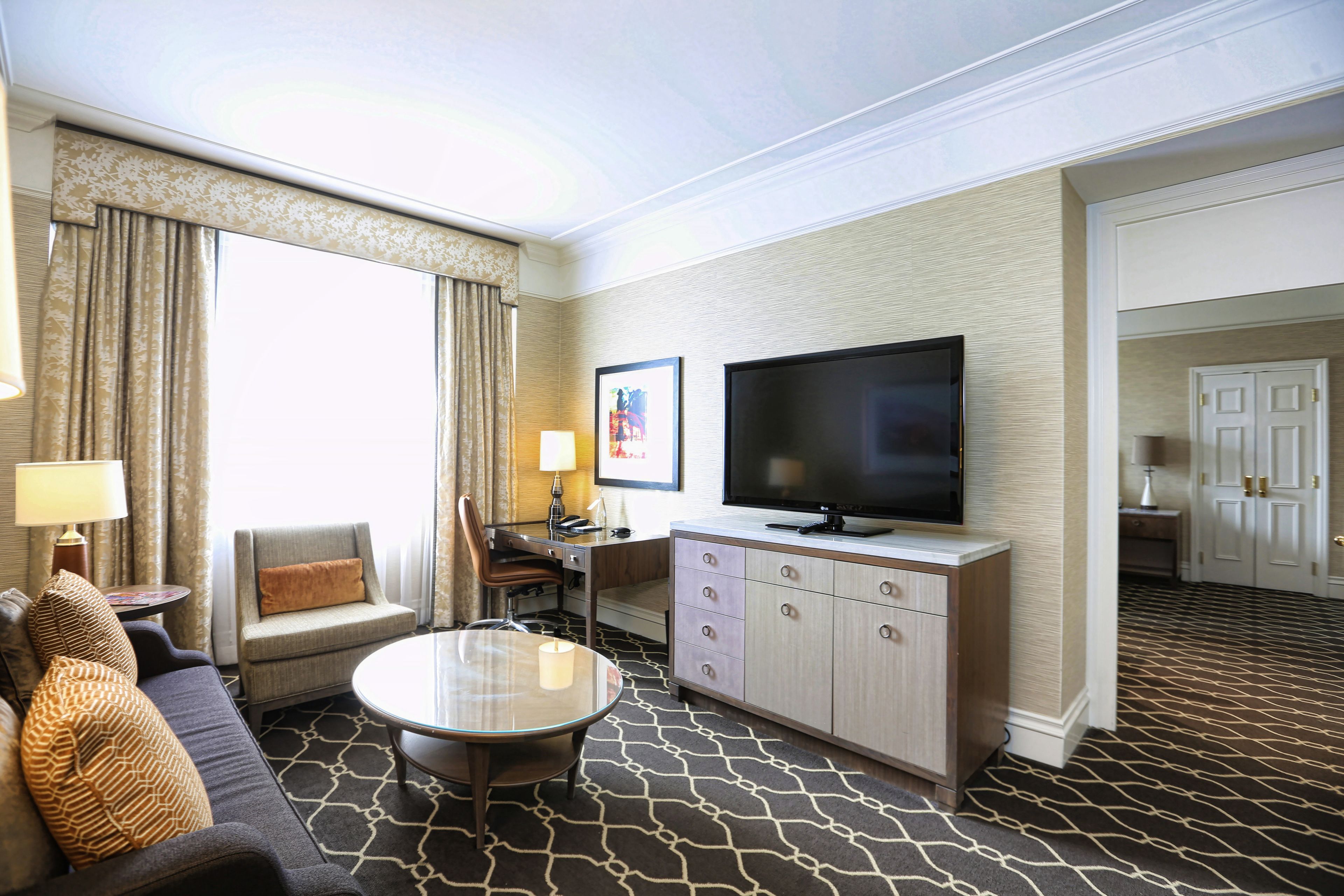 A hotel room with a sofa, armchair, dining table, TV, and a cabinet.
