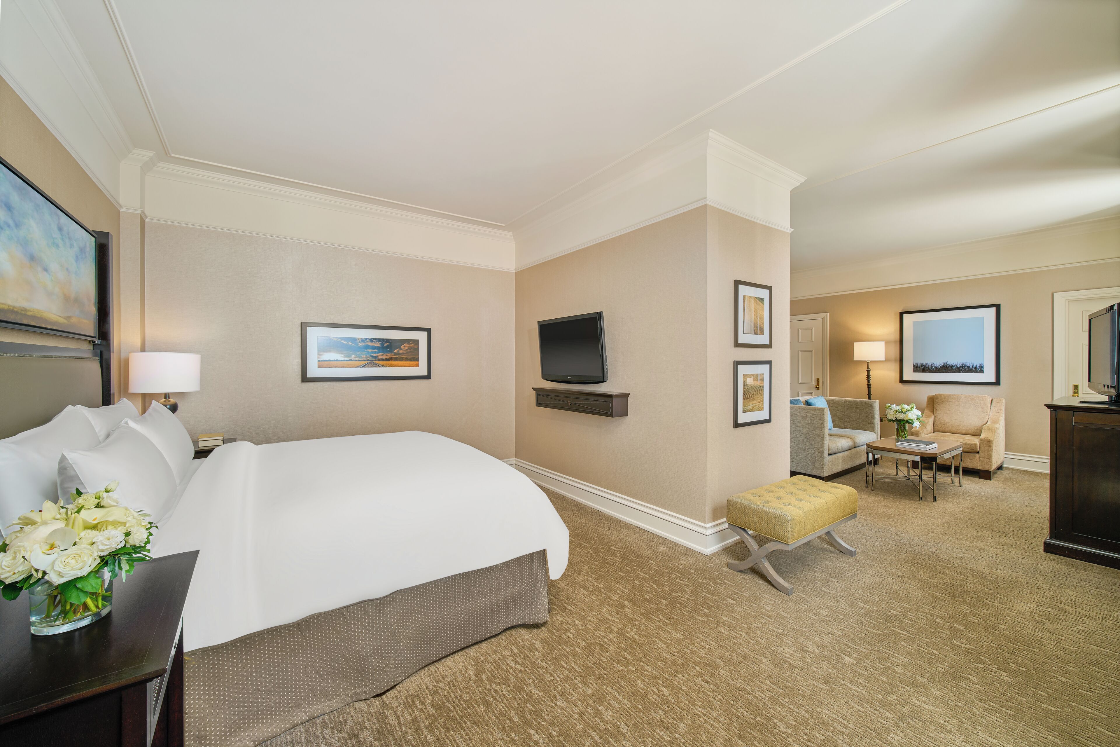 Een hotelkamer met een groot bed, een televisie, een bureau met lamp, een stoel en een kleine tafel met bloemen.