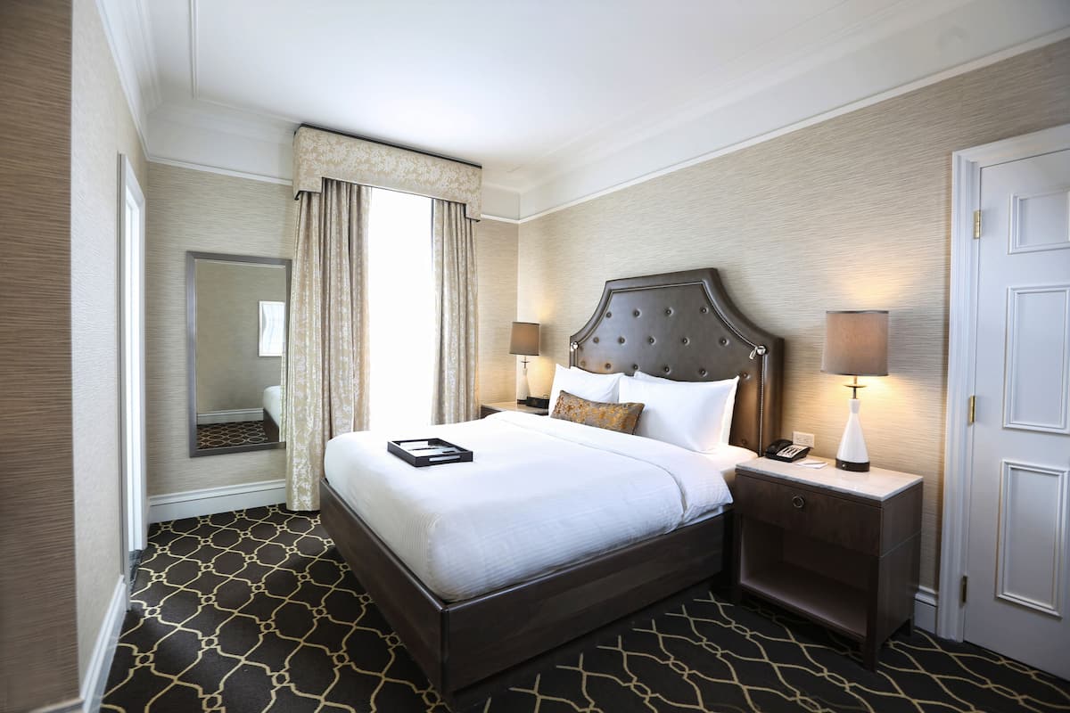 A hotel room with a large bed, two bedside tables, a nightstand, a mirror, and a door.
