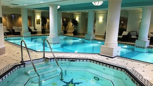 Una amplia piscina interior con un suelo estampado con motivos de estrellas, rodeada de columnas y sillones de descanso.