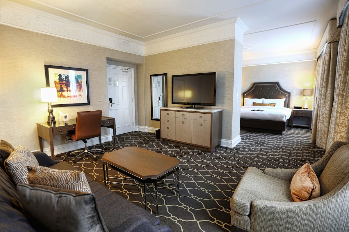 A hotel room with a sofa, armchair, desk, television, and a bed.