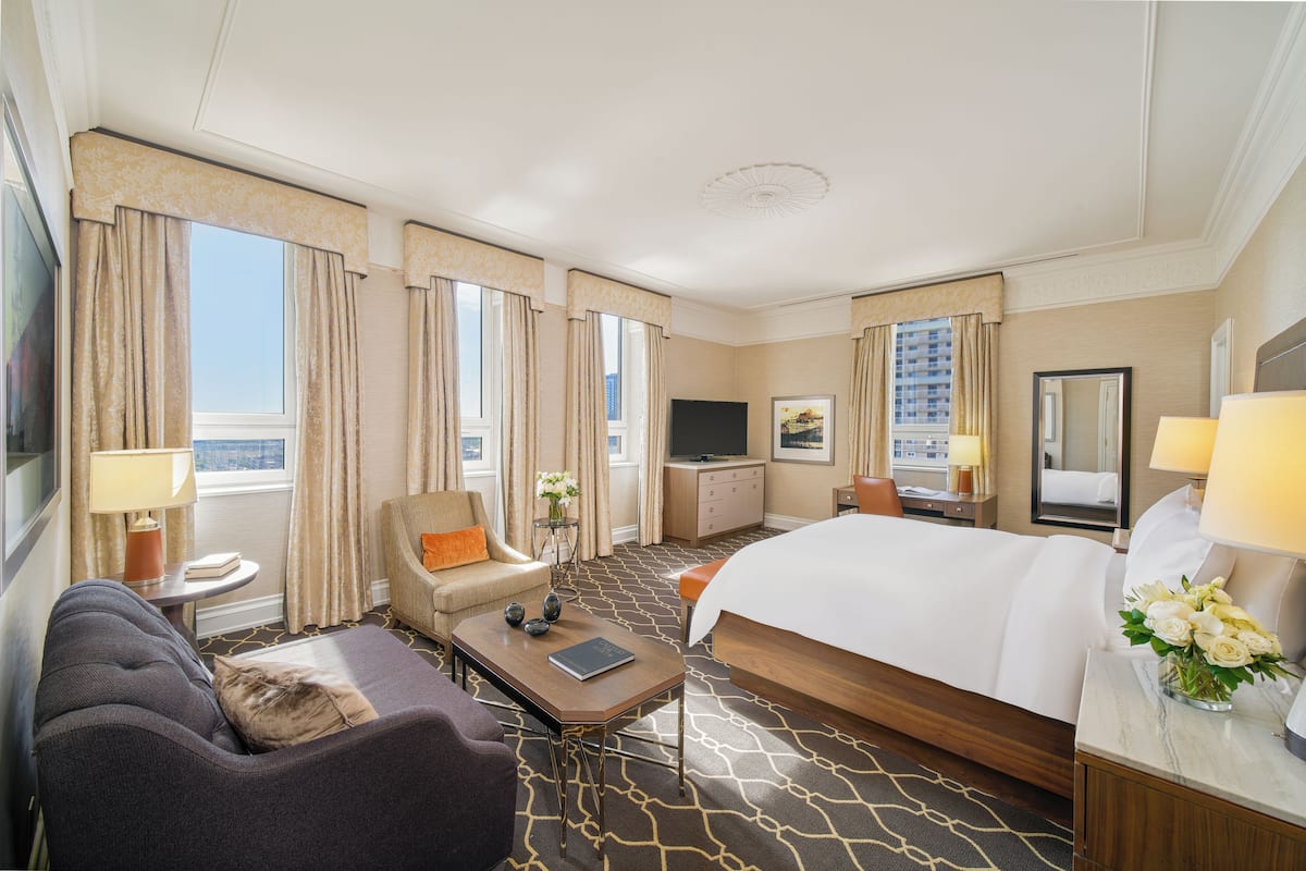 A hotel room with a bed, a sofa, a desk, a TV, a dresser, and a window with curtains.