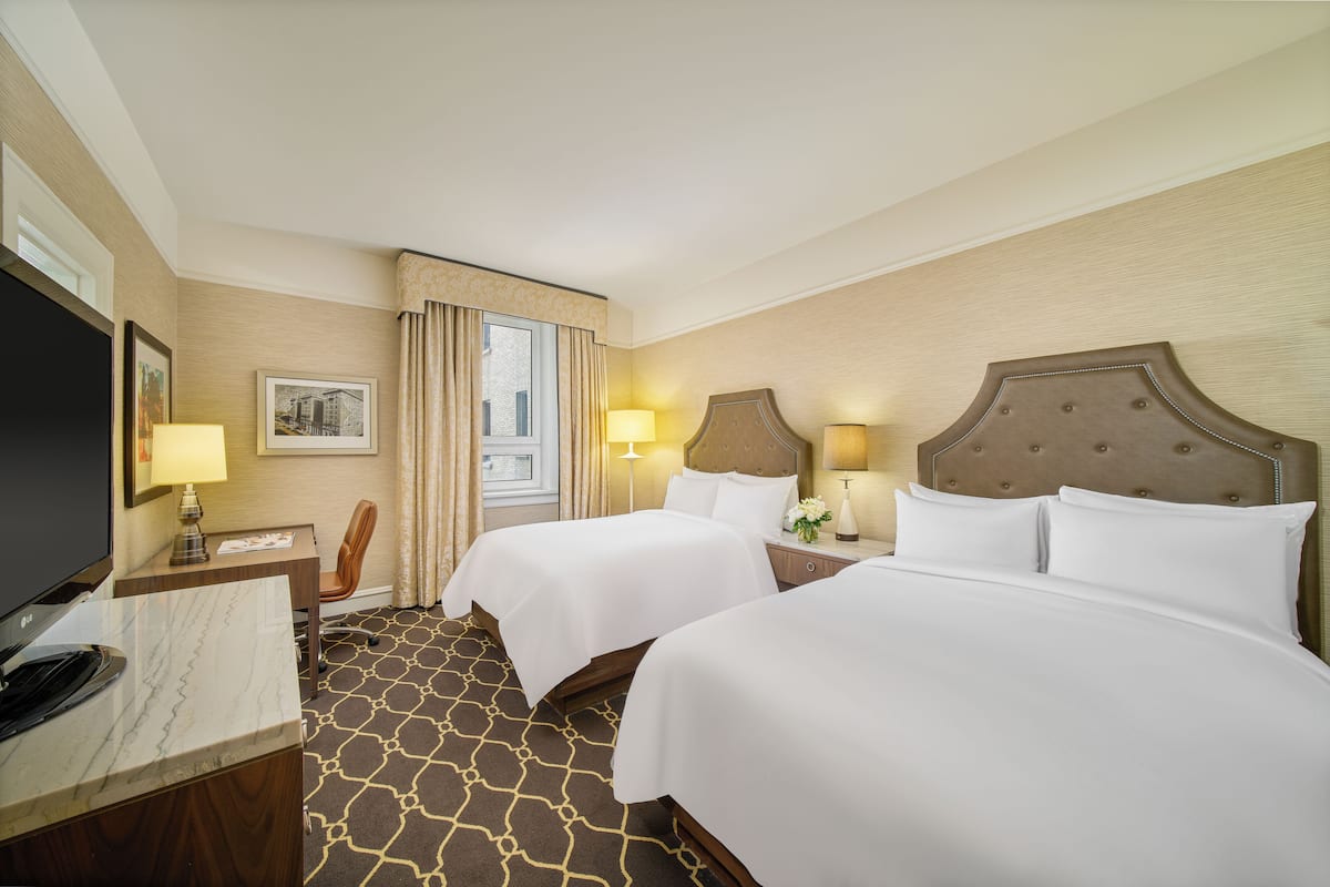 A hotel room with two beds, a desk with a television, and a window with curtains.
