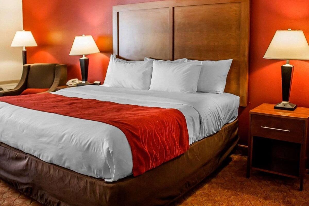 Una habitación de hotel con una cama grande, dos mesitas de noche, una silla y una pared decorada en rojo.