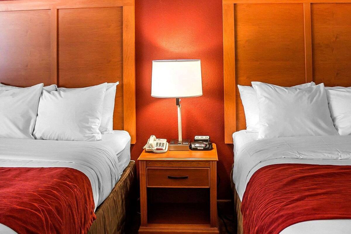 Una habitación de hotel con dos camas, una mesita de noche con lámpara, teléfono y un cajón pequeño.