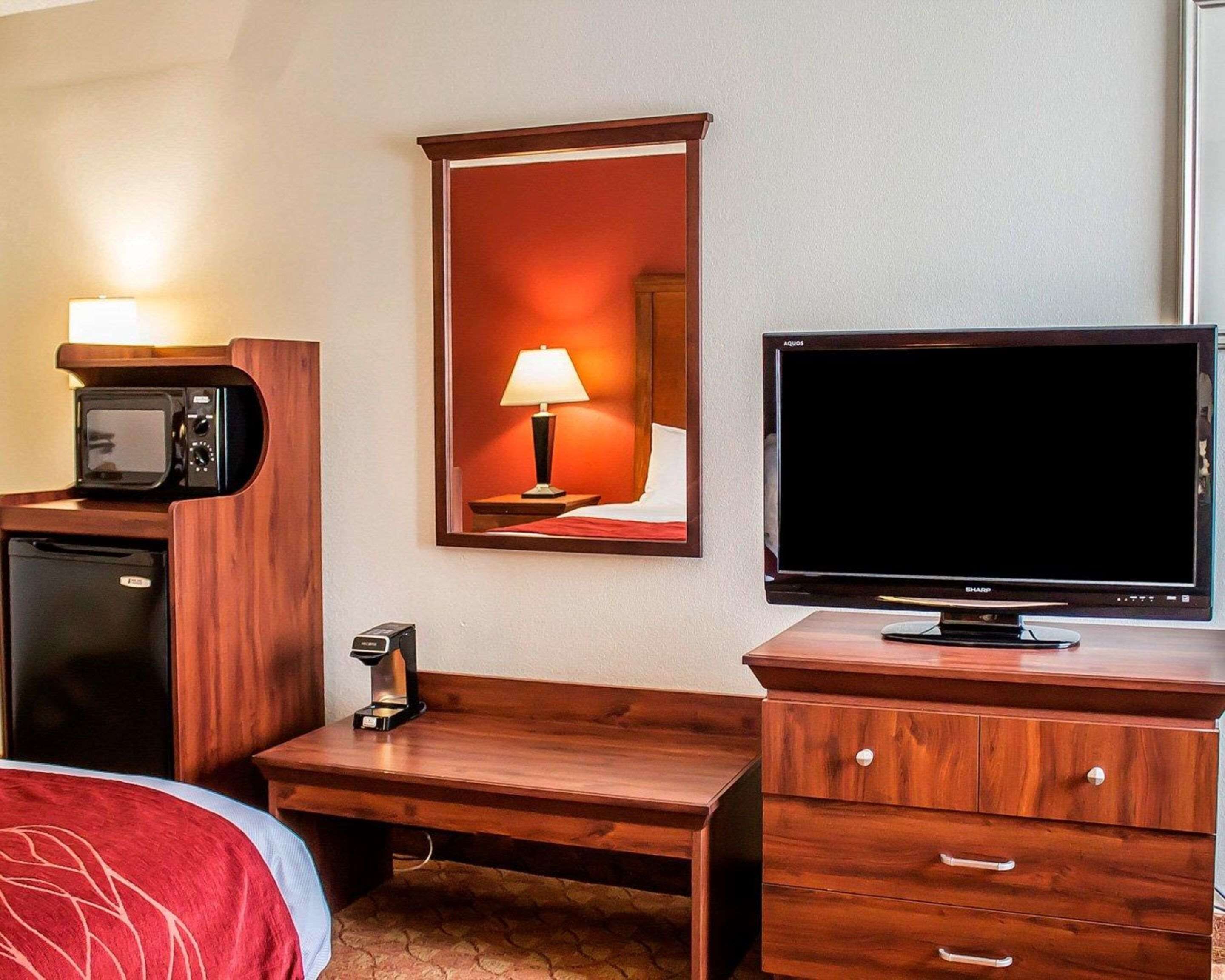 A hotel room with a bed, a wooden desk, a television, a microwave, a coffee maker, and a mirror.