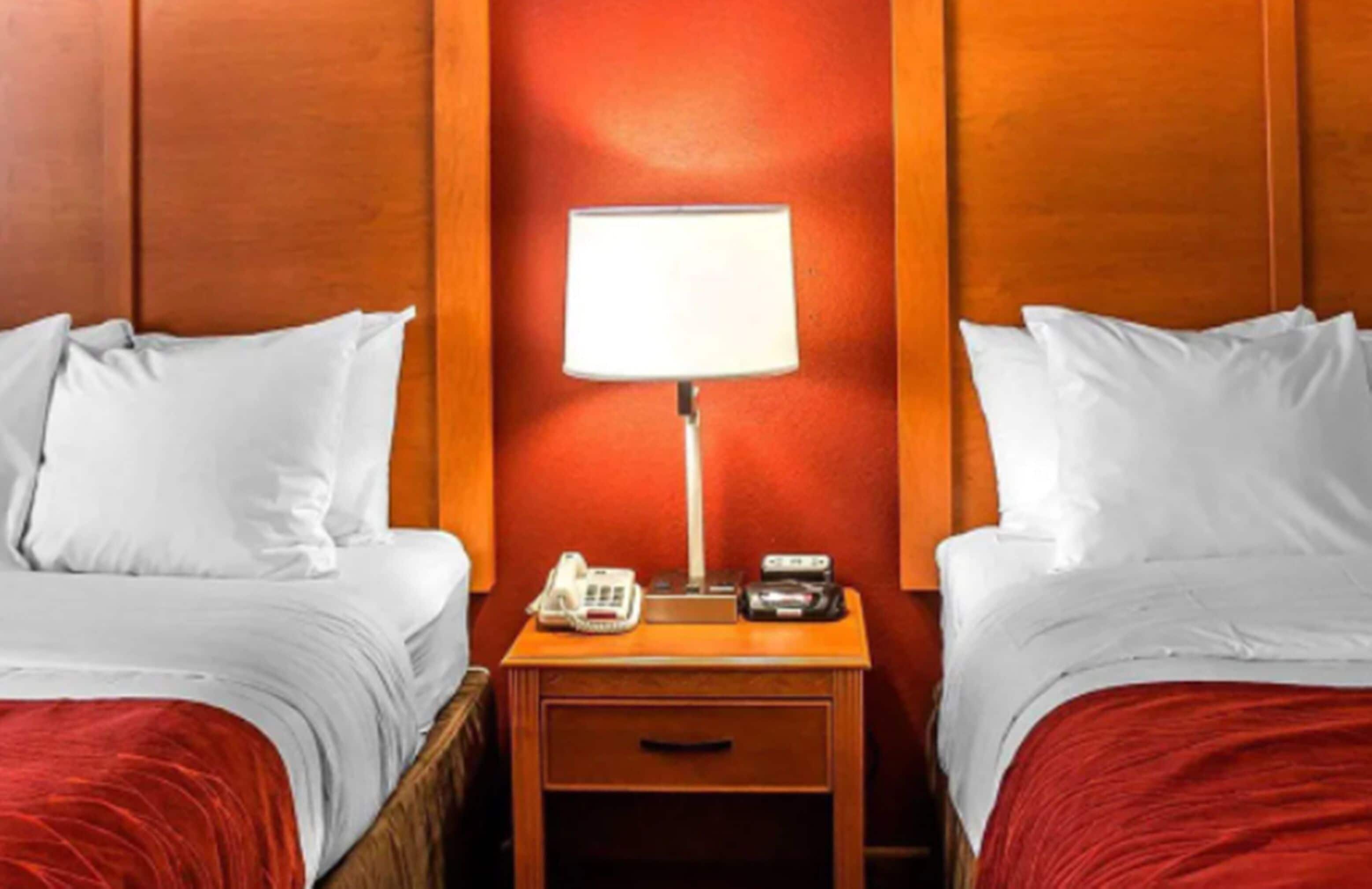 A hotel room with two beds, a nightstand with a lamp, a phone, and a radio.