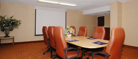 A conference room with a large table, six chairs, a projector screen, and a floral arrangement.