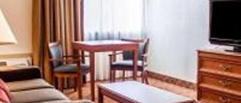 Habitación de hotel con sofá, una mesita, televisor y ventana con cortinas.